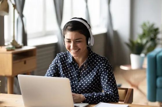 Happy indian young girl student wear headphone watch webinar listen online course communicate by conference video call e learn language in app laugh study with teacher lesson look at laptop at home